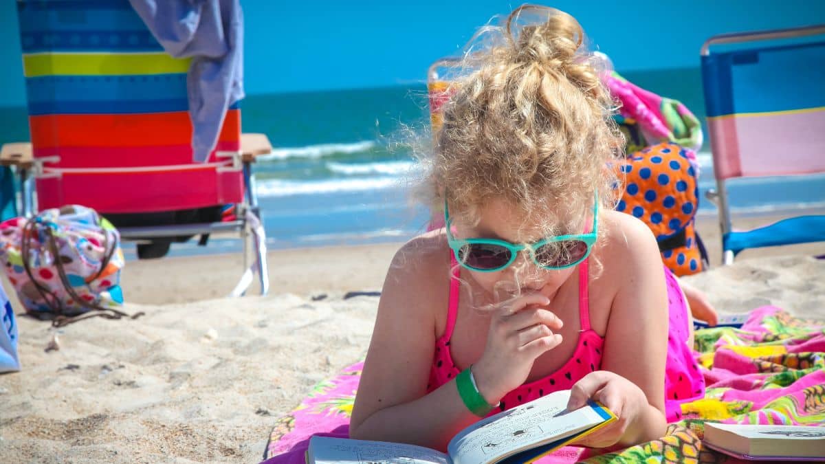 Una niña lee su cuaderno en una playa durante el verano