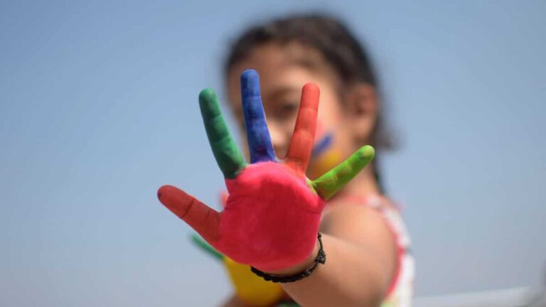 Una niña con una mano pintada con tempera durante el verano